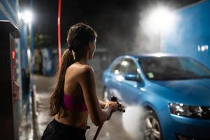 mujer joven lavando un auto azul en un lavadero de autos foto