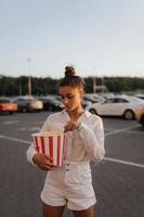 linda mujer joven sosteniendo palomitas de maíz en el estacionamiento de un centro comercial foto