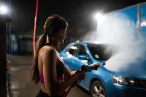 mujer joven lavando un auto azul en un lavadero de autos foto