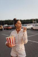 linda mujer joven sosteniendo palomitas de maíz en el estacionamiento de un centro comercial foto