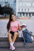 Cheerful young woman taking notes while sitting on steps otdoors photo