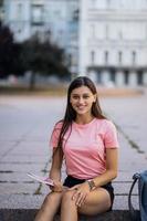 una joven alegre tomando notas mientras se sienta en los escalones al aire libre foto