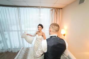 Pillow fight of bride and groom in a hotel room photo