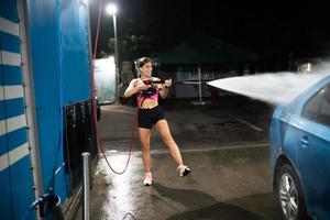 Young woman washing blue car at car wash photo