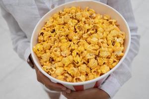 Close-up photo of a young sweet girl, who is holding a tube of popcorn in her hands.