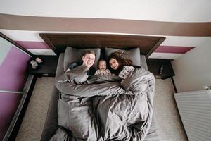 niño feliz con los padres en la cama en casa foto