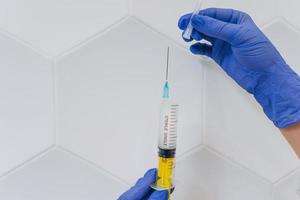 Hands in rubber gloves hold a disposable medical syringe with the drug photo