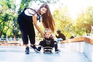 joven madre le enseña a su hijo pequeño a andar en patineta foto