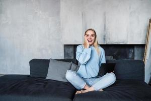 Image of happy woman using silver laptop while sitting on sofa photo