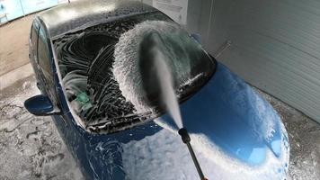 Young man spraying down his car with soapy water photo