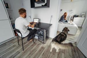 Dad works at laptop, mom and baby on the bed photo