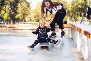 joven madre le enseña a su hijo pequeño a andar en patineta foto