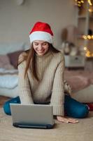Female wearing santa hat while speaking with online friend on laptop photo