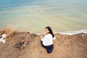 attractive woman in summer skirt and shirt sits on the shore photo