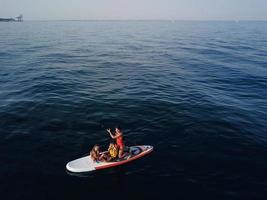 Mother with two daughters stand up on a paddle board photo