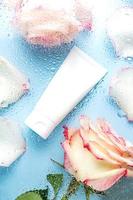 cosmetic tube for face cream, cleanser or body lotion on a blue background with water droplets and rose flowers through the glass. The concept of a moisturizing cosmetic product photo