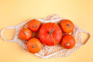 Ripe pumpkins in mesh bag on yellow background. Autumn harvest and Thanksgiving concept. Eco-friendly farm products. photo