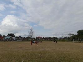 mataram city, isla de lombok, indonesia, 4 de septiembre de 2022, niños practicando fútbol en un campo de fútbol con hierba seca foto