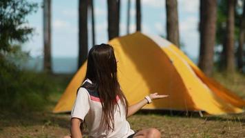 una joven se sienta en una alfombra de yoga fuera de una carpa amarilla en el campamento video