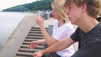 Teen boy and girl with backpacks and skateboard stand and talk in sunny outdoor city space video