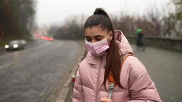 jong vrouw in roze jas en masker gegroet een auto van de trottoir video