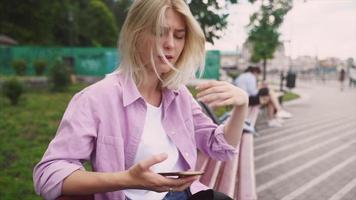 blond tiener- meisje toepassingen slim telefoon terwijl rennen een hand- door haar haar- vervolgens looks Bij camera met een kalmte glimlach video