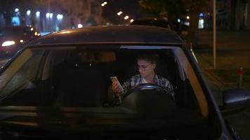 niña sentada en un auto estacionado usando un teléfono inteligente en la noche video