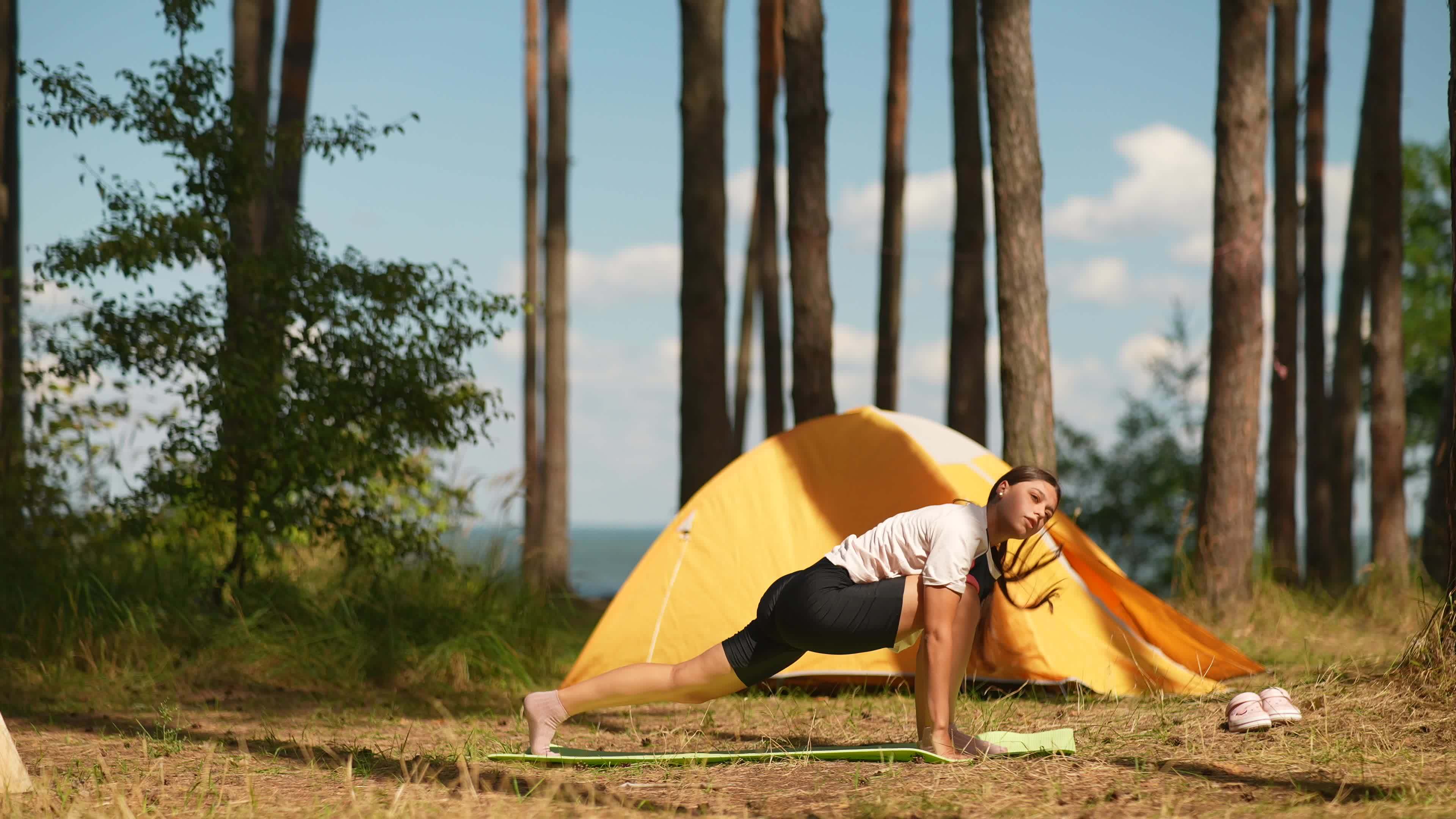 Young woman stretches on a yoga mat outside a yellow tent at camp site  11482922 Stock Video at Vecteezy