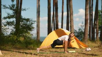 Young woman stretches on a yoga mat outside a yellow tent at camp site video