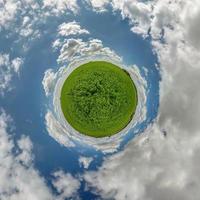 green tiny planet in blue sky with beautiful clouds. Transformation of spherical panorama 360 degrees. Spherical abstract aerial view. Curvature of space. photo