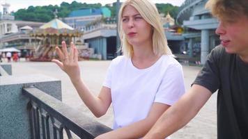 Teen boy and girl with backpacks and skateboard stand and talk in sunny outdoor city space video