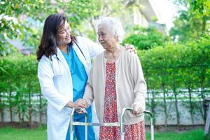 Doctor help Asian elderly woman disability patient walk with walker in park, medical concept. photo