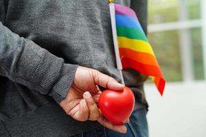 mujer asiática sosteniendo hert rojo con bandera del arco iris, derechos de símbolo lgbt e igualdad de género, mes del orgullo lgbt en junio. foto