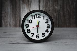 Black alarm clock isolated on wooden desk. The clock set at half past twelve. photo