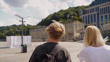 tonåring pojke och flicka med ryggsäckar och skateboard stå och prata i solig utomhus- stad Plats video