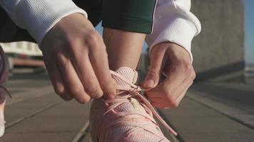 Woman laces up pink running shoes on sidewalk video