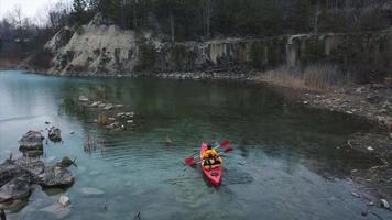 People in orange kayak paddle in flooded rock quarry video