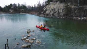 People in orange kayak paddle in flooded rock quarry video