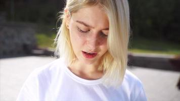 Young blonde woman or teen looks up at camera in bright sunshine video