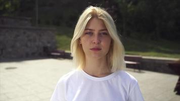 Young blonde woman or teen looks up at camera in bright sunshine video