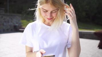 Young blonde woman or teen looks up at phone texting in bright sunshine video