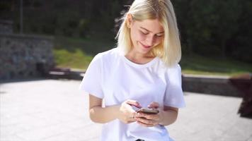 joven rubia o adolescente mira hacia arriba a los mensajes de texto del teléfono bajo el sol brillante