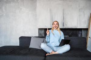 Image of happy woman using silver laptop while sitting on sofa photo