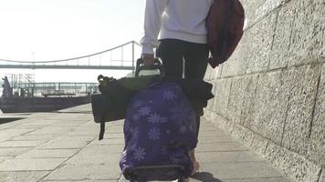 Woman in white sweatshirt carries luggage bags down sidewalk video