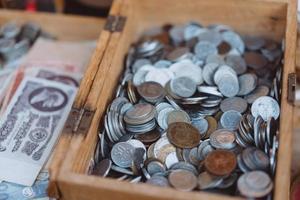 Old coins of different denominations are in a small wooden box photo