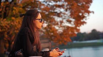 mujer mira el teléfono inteligente en una parte con agua y follaje de otoño video