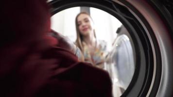 vue depuis l'intérieur de la sécheuse alors qu'une femme jette le linge et les vêtements tombent video