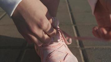 Woman ties pink tennis shoe before outdoor exercise video