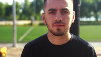 Young man looks intensely at camera from side of outdoor sports field video