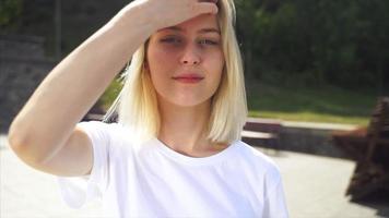 jong blond vrouw of tiener looks omhoog Bij camera en loopt hand- door haar- in helder zonneschijn video
